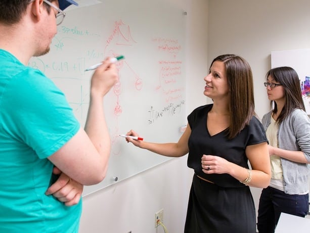 Blythe Adamson whiteboards a problem in health economics research with colleagues Nathaniel Hendrix, left, and Wei-Jhih Wang.